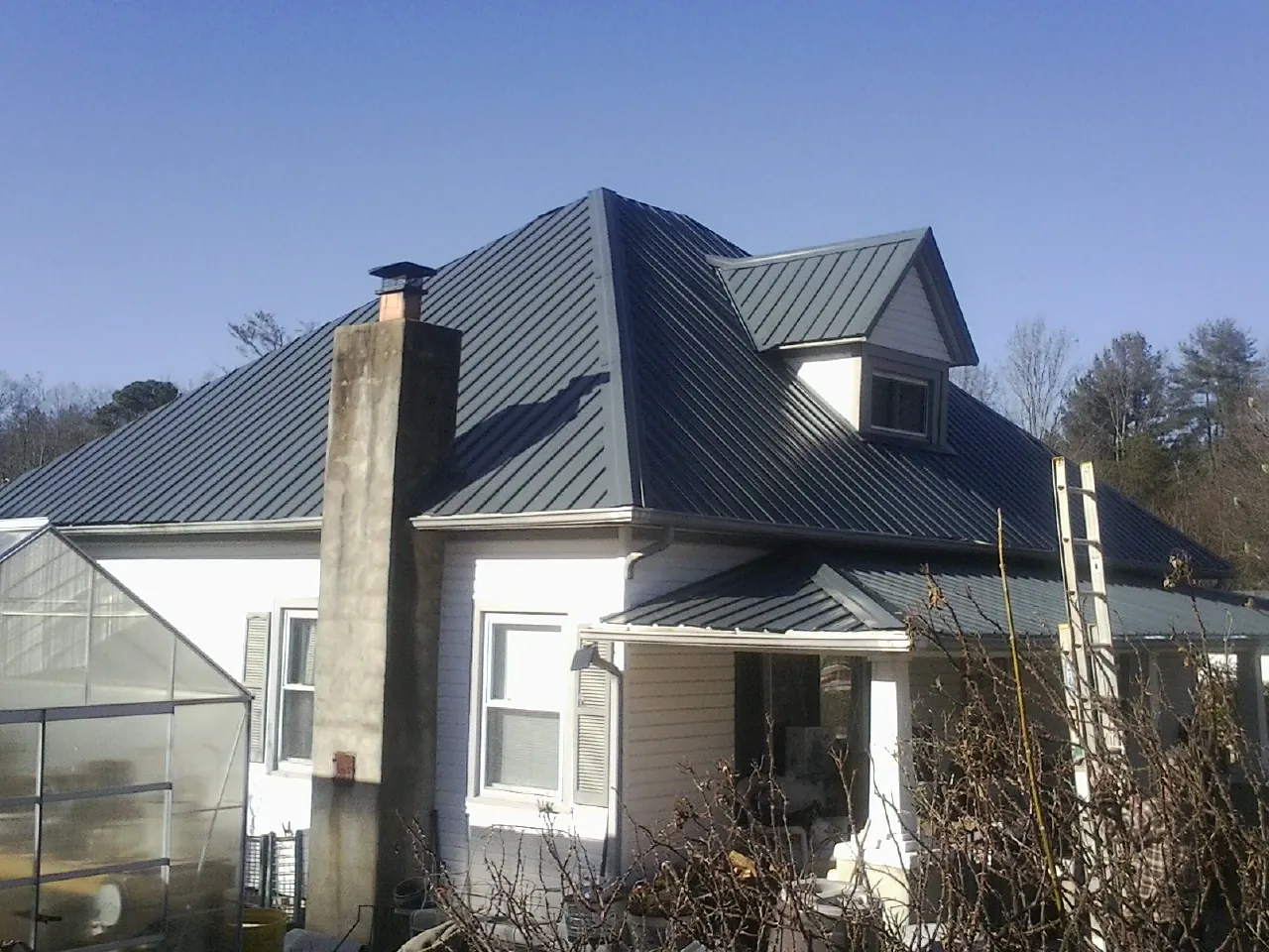 Dark blue standing seam metal roof on a white farmhouse with dormer — Slate & Tile Roof Repair by Roofing Brothers in Wolflake