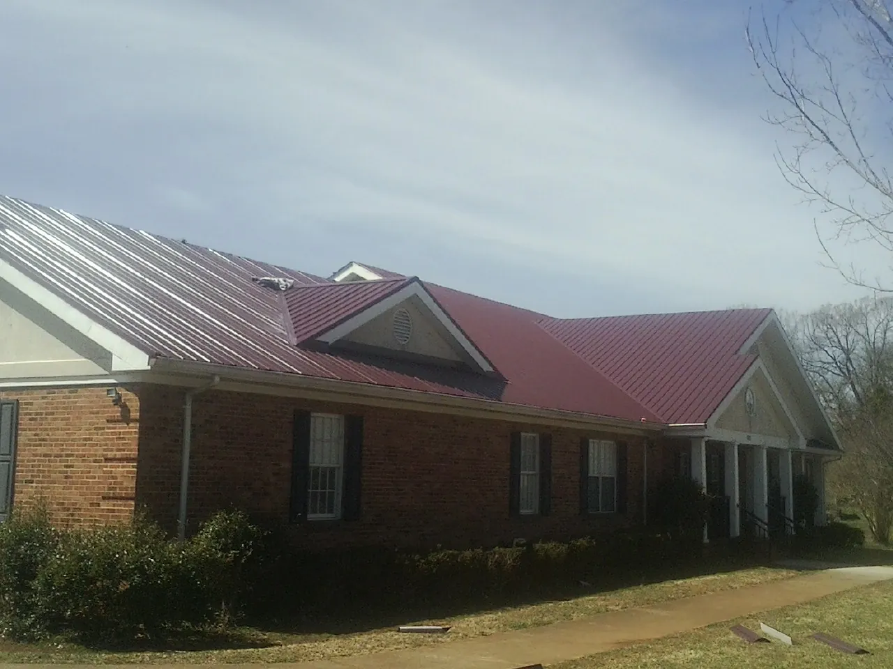 Red metal roof with gabled entries on a long brick building, from a Hail Damage Roof Repair job in Wolflake
