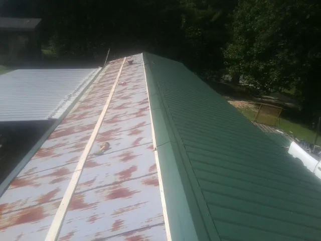 Old rusted panels beside newly installed green metal roofing — Wind Damage Roof Repair by Roofing Brothers in Wolflake