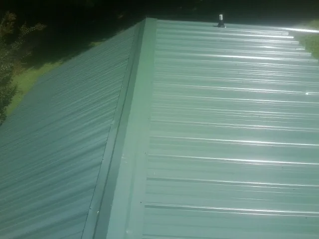New green metal panels meeting at the ridge of a roof — Flat Roof Repair work by our crew in Wolflake