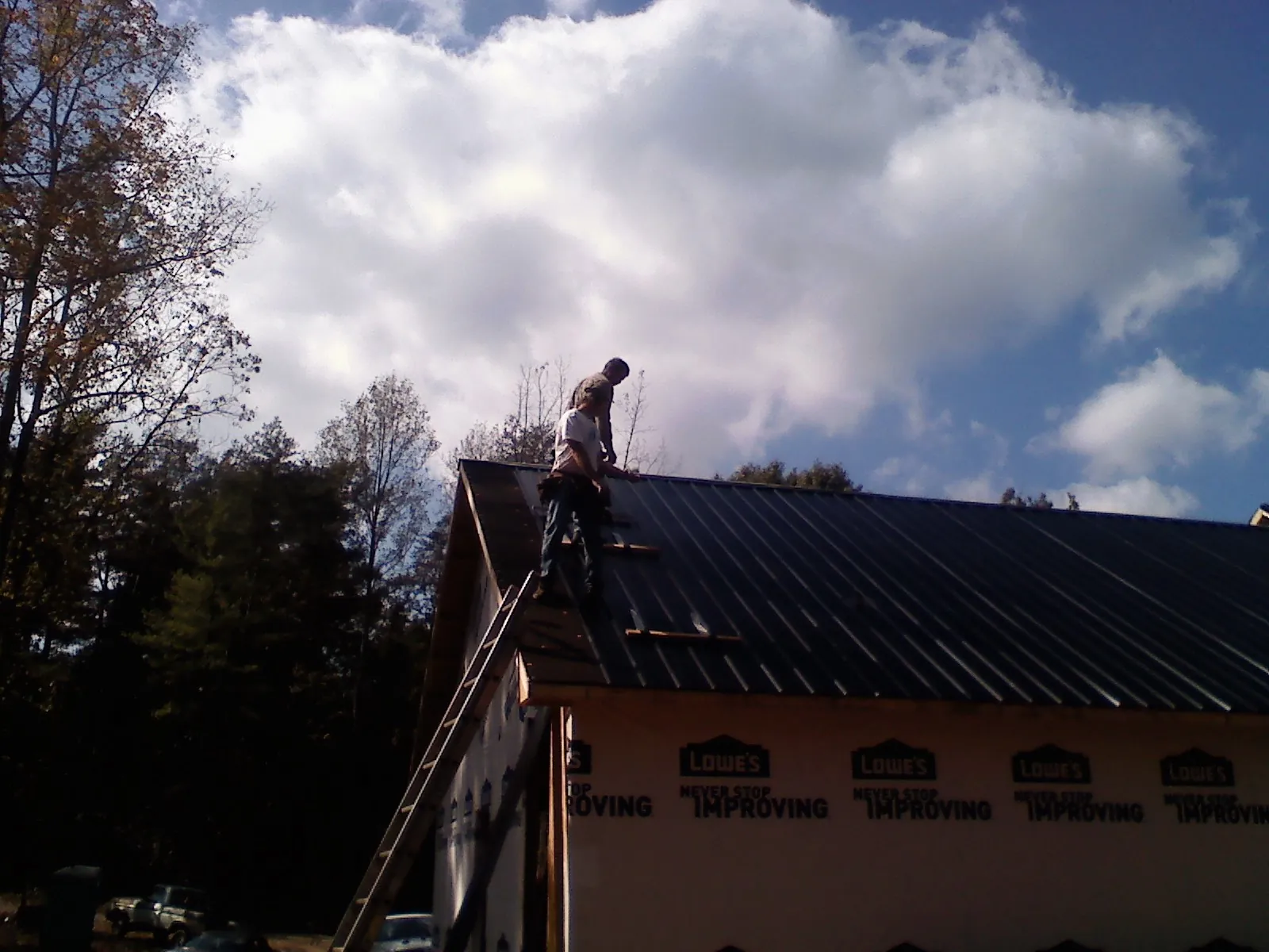 Roofer fastening dark metal panels high against a cloudy sky, from a Roof Inspection job in Wolflake